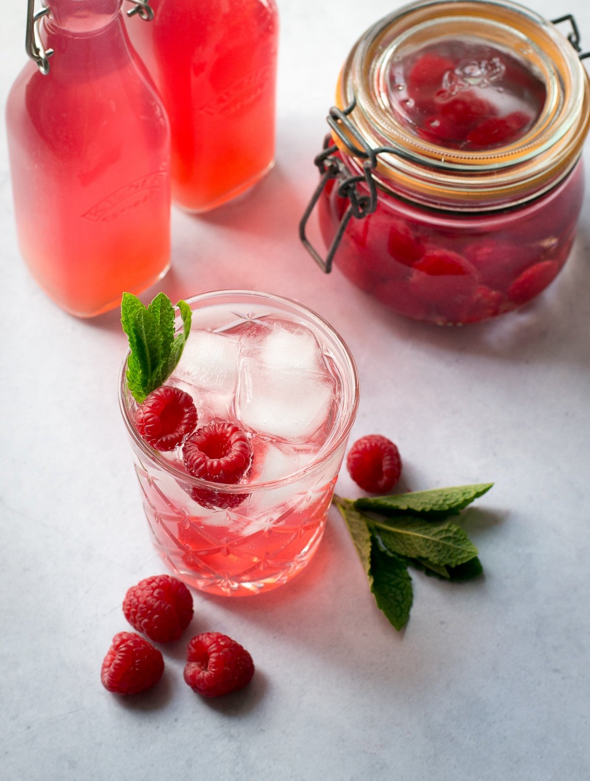 A glass of raspberry gin with preserving jar